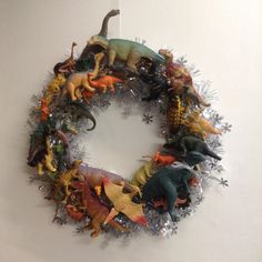 a wreath made out of plastic dinosaurs and other toy animals is hanging on the wall