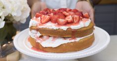 a cake with strawberries on top is sitting on a plate next to a flower vase