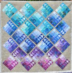 a quilted wall hanging on the side of a building with lots of blue and purple squares