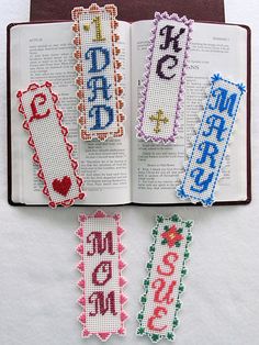 four cross stitch bookmarks are placed on top of an open book with the word love written in it