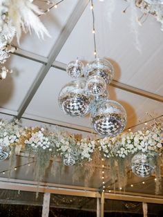 several disco balls hanging from the ceiling with white flowers and greenery in front of them