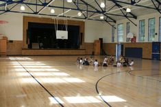 some kids are sitting on the floor in a gym with basketball hoops and chairs