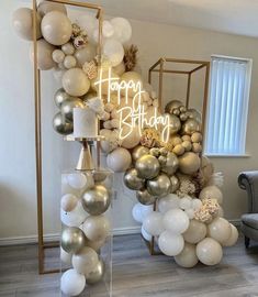 balloon arch with happy birthday sign surrounded by white and gold balloons in a living room