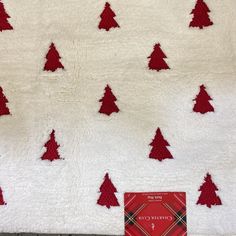 a white blanket with red christmas trees on it next to a small book that is laying on the floor