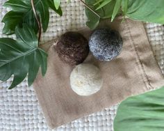 three balls of wool sitting on top of a cloth next to green leafy plants