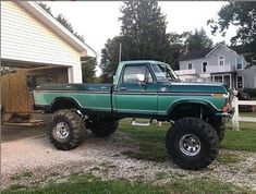 a green pick up truck parked in front of a house with large tires on it