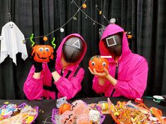 two people in pink costumes are holding pumpkins