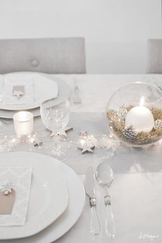 a table set with white plates and silverware, candles and napkins on it