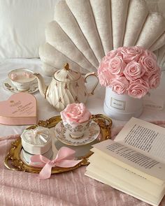 there is a tray with pink roses on it and tea set next to an open book