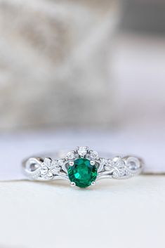 an emerald and diamond ring sitting on top of a white surface with a stone in the background