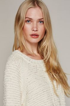 a woman with long blonde hair wearing a white sweater and blue eyes is looking at the camera