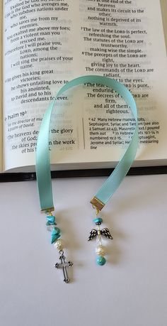 an open book with a blue ribbon around it and two charms hanging from the front