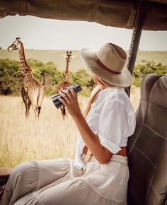 a woman is sitting on the back of a vehicle looking at giraffes