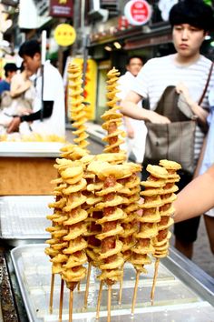 several skewered food items on sticks in front of people at an outdoor market