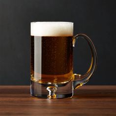 a glass mug filled with beer sitting on top of a wooden table next to a black wall