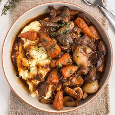 a bowl filled with meat and potatoes covered in gravy on top of a table