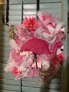 a pink flamingo wreath hanging on the side of a blue door with flowers in it