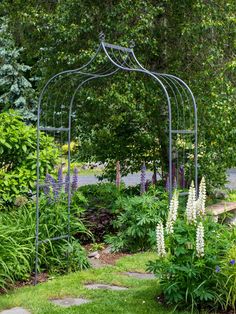 a garden with lots of flowers and plants around it, including an iron trellis