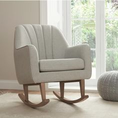 a white rocking chair sitting in front of a window next to a gray ball on the floor