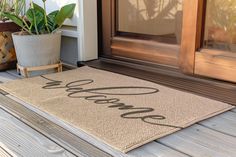 a welcome mat sitting on the front porch with potted plants next to it that says welcome