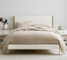 a white bed with two nightstands and a vase on the end table next to it