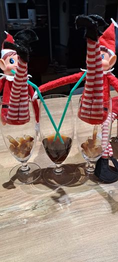 three wine glasses sitting on top of a table next to each other with elf figures in them