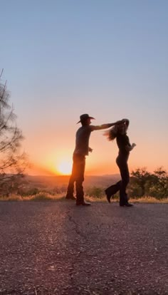 two people standing on the side of a road with their arms around each other as the sun sets