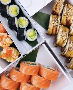 sushi and other food items are displayed in separate trays on a white surface