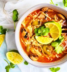 a bowl of chicken noodle soup with limes and cilantro