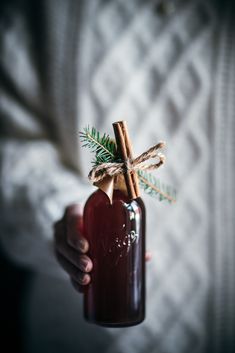 a person holding a bottle with cinnamon sticks in it and a stick sticking out of it