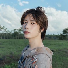 a young man standing in front of a lush green field under a cloudy blue sky