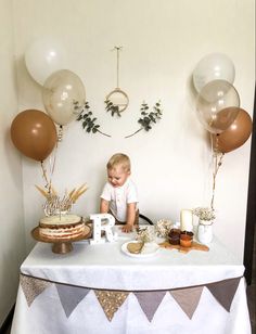 a little boy sitting at a table with some balloons and cake on top of it