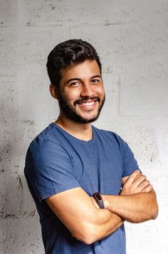 a man standing with his arms crossed in front of a white brick wall smiling at the camera