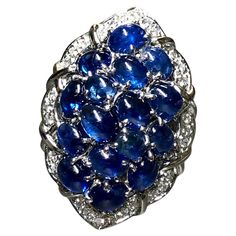 An incredibly colorful cocktail ring crafted in platinum and set with approximately 11.50cttw in vibrant royal blues cabochon sapphires surrounded by approximately .50cttw in G-H color Vs1-2 clarity round diamonds. A gorgeously made and substantial ring that you will absolutely know that you have on; it makes quite the statement! Dimensions/Weight: Ring measures 1.25” by .95” and weighs 23.8g. Size 7 (sizable). Condition: All stones are secure and in perfectly wearable condition. R-BCYYE Luxury Sapphire Ring With Cabochon, Vintage Cocktail Ring, White Gold Sapphire, Diamond Cocktail Rings, Fancy Diamonds, Sapphire Diamond Ring, Ring Crafts, Sapphire Stone, Pearl Diamond