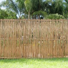 a wooden fence made out of bamboo sticks in the middle of a grassy area with trees and bushes behind it