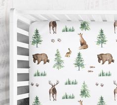 a baby crib with deer and bear wallpaper on the side, along with pine trees