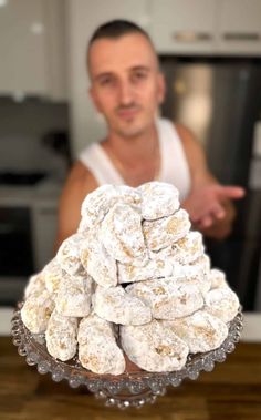 a man standing in front of a glass bowl filled with powdered sugar coated doughnuts