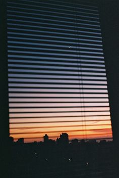 the sun is setting in front of a window with vertical blinds on top of it