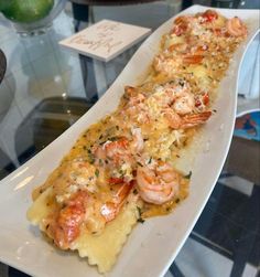 a long white plate topped with shrimp and cheese covered in sauce on top of a glass table