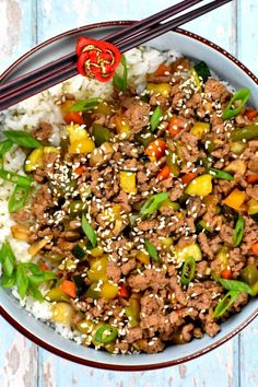 a bowl filled with meat and vegetables on top of rice next to chopsticks