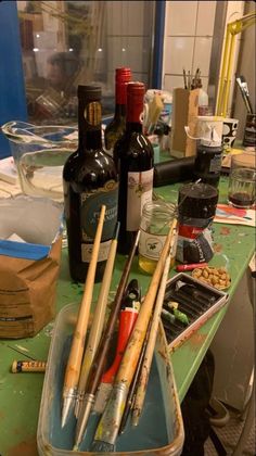 the paintbrushes are sitting on the table next to wine bottles and other art supplies