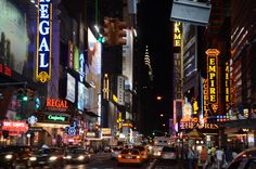 a busy city street at night with neon signs and people walking on the sidewalk in the foreground