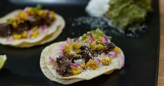 three small tortillas on a black plate with lime wedges and other toppings