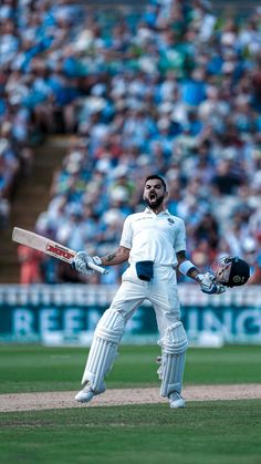 a man holding a cricket bat standing on top of a field in front of a crowd