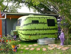 a large green trailer parked next to a tree filled yard with potted plants on it