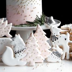 a cake with white frosting and decorated christmas trees on the side next to cookies