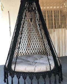 a black hanging bed with tassels on the sides and a white pillow underneath it