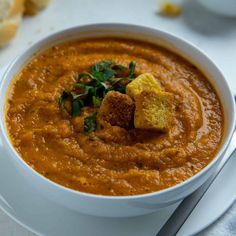 a white bowl filled with carrot soup and croutons