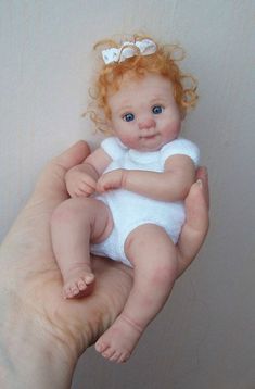 a hand holding a small doll in it's right hand and wearing a white bodysuit