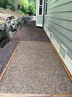 a gravel path leading to a house with rocks on the side and grass in front